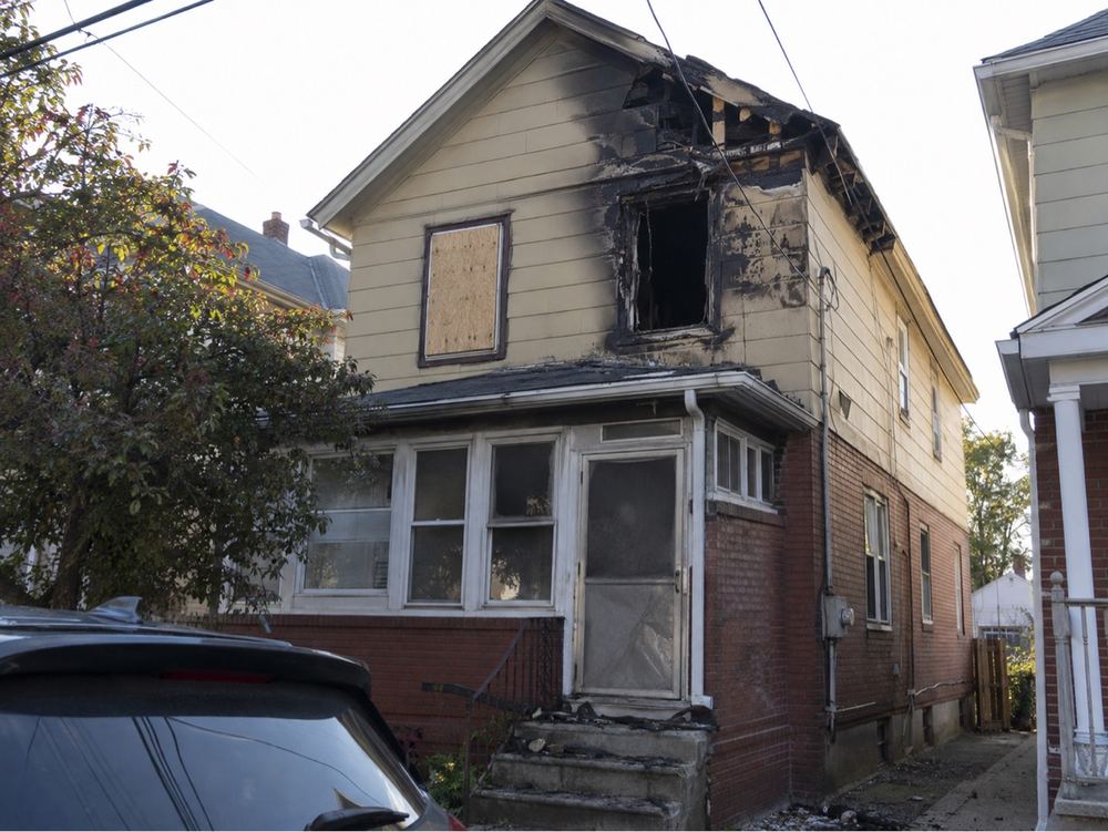 Two-family house with fire damage and a boarded window.
